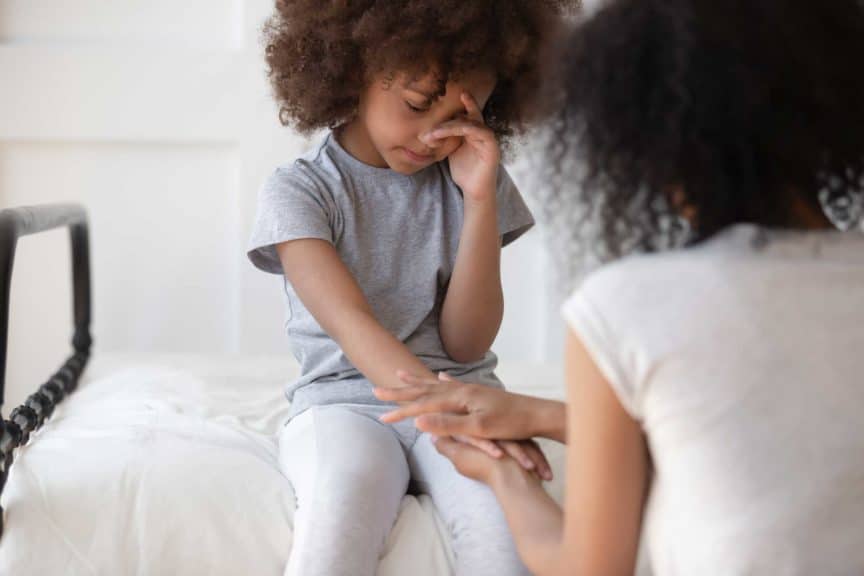 mommy holding hand of upset little cute girl sitting on bed