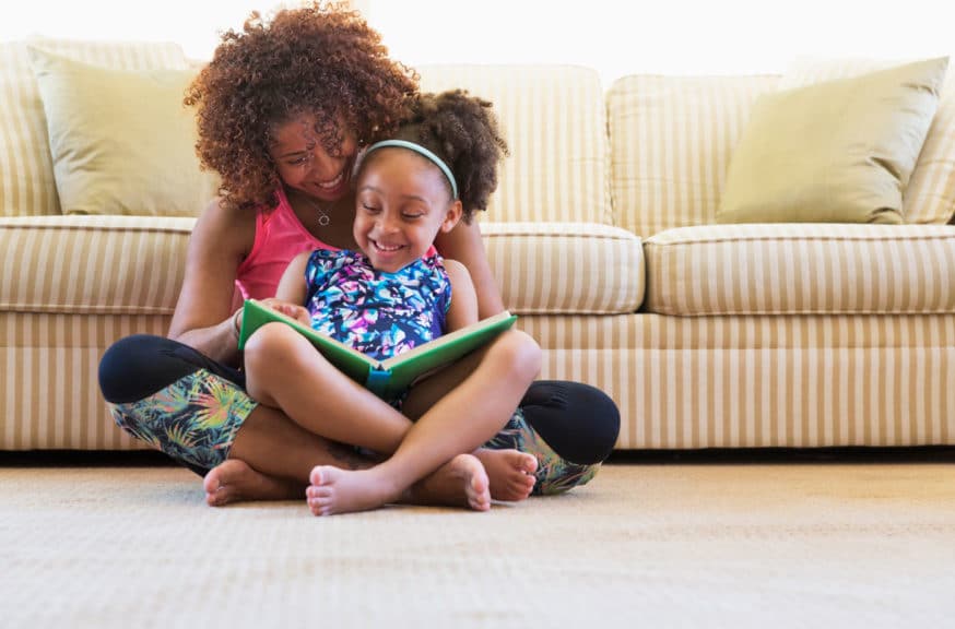 mother and daughter reading book on floor near sofa