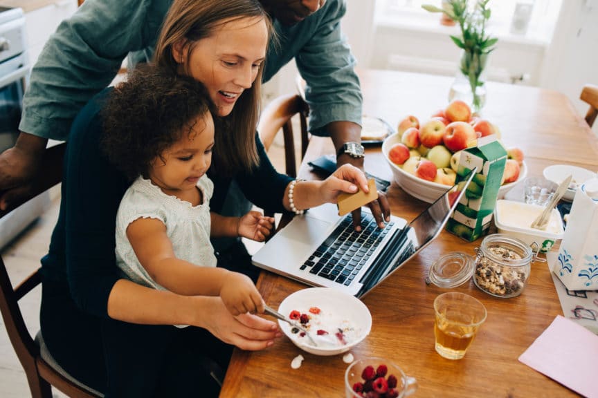 Parents shopping online on laptop while looking at daughter having breakfast in dining room