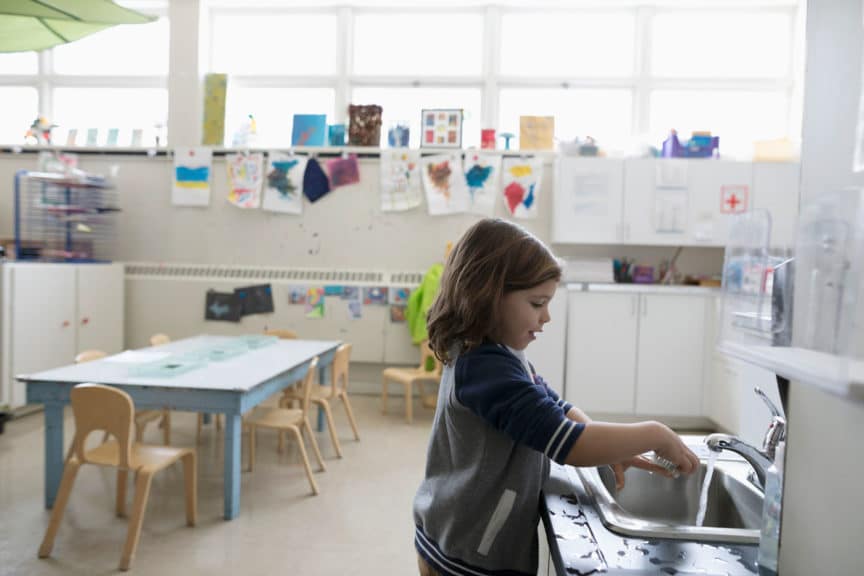 Preschool girl washing hands at sink in classroom