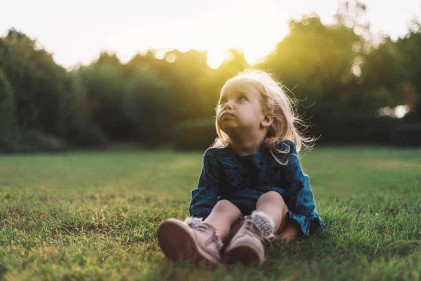 Portrait of a sad little girl looking away with sad facial expression by sitting in a public park