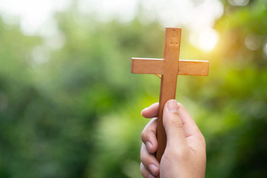 Silhouette of human hands praying to the GOD while holding a crucifix symbol