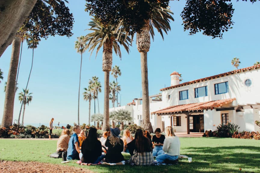 Students outside meeting in a circle on lawn on sunny day