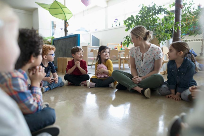 children sitting on the floor in a circle with their teacher