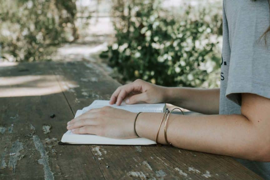 Teen girl reading bible outdoors on table