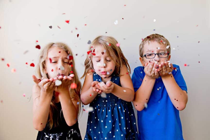 three children blowing confetti at camera