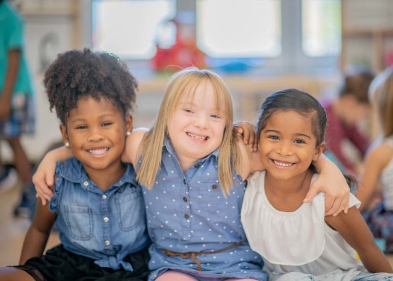 Three girls hugging friends at kindergarten