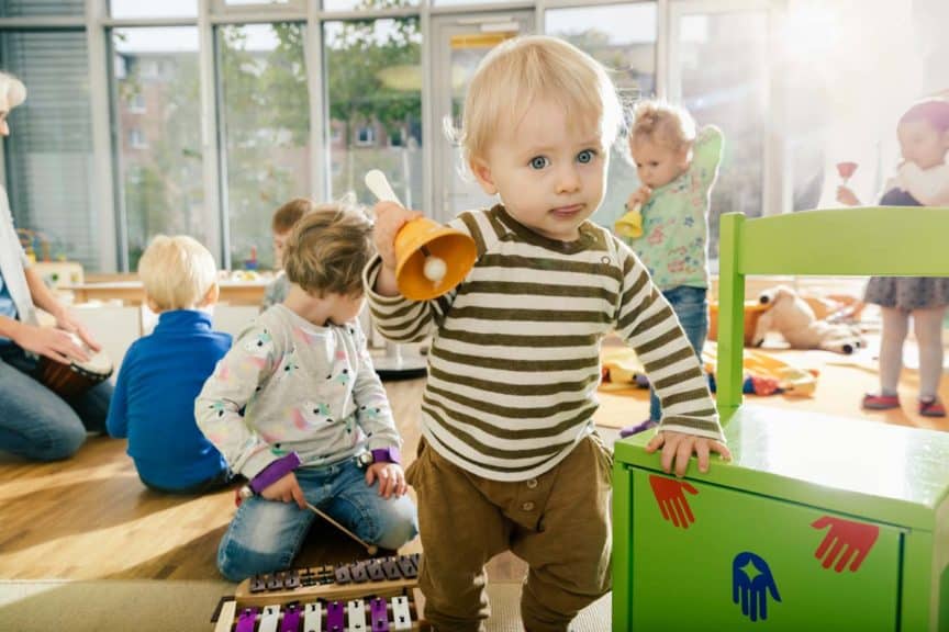 Toddler ringing a bell in music room of a kindergarten