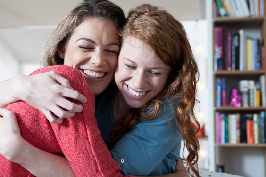 Two young female friends at home embracing