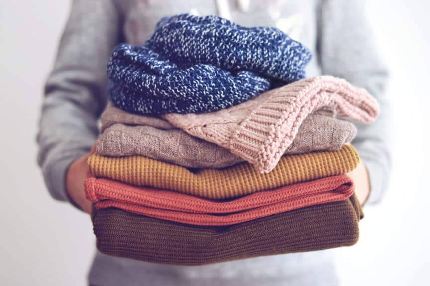 Woman holding fall color sweaters